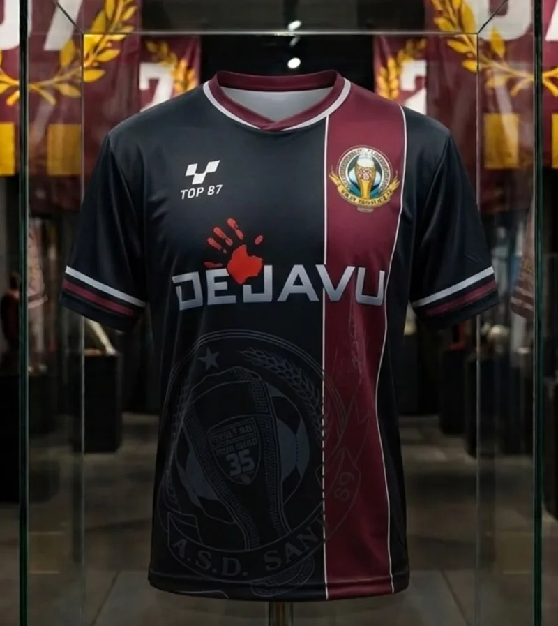 Maglia nera con una banda verticale granata, lo stemma in trasparenza e lo sponsor Dejavu.