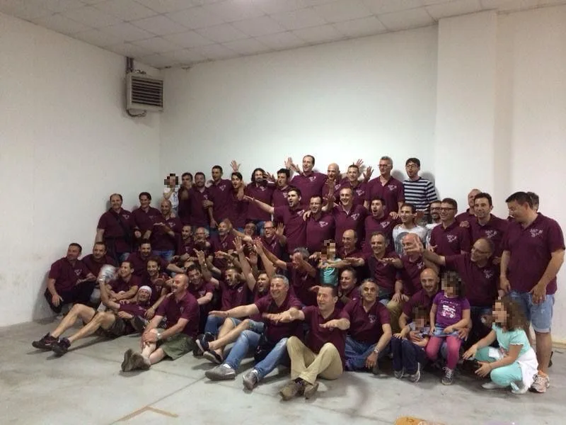 Foto di gruppo di giocatori, dirigenti e famiglie in polo granata, molti con le braccia alzate.